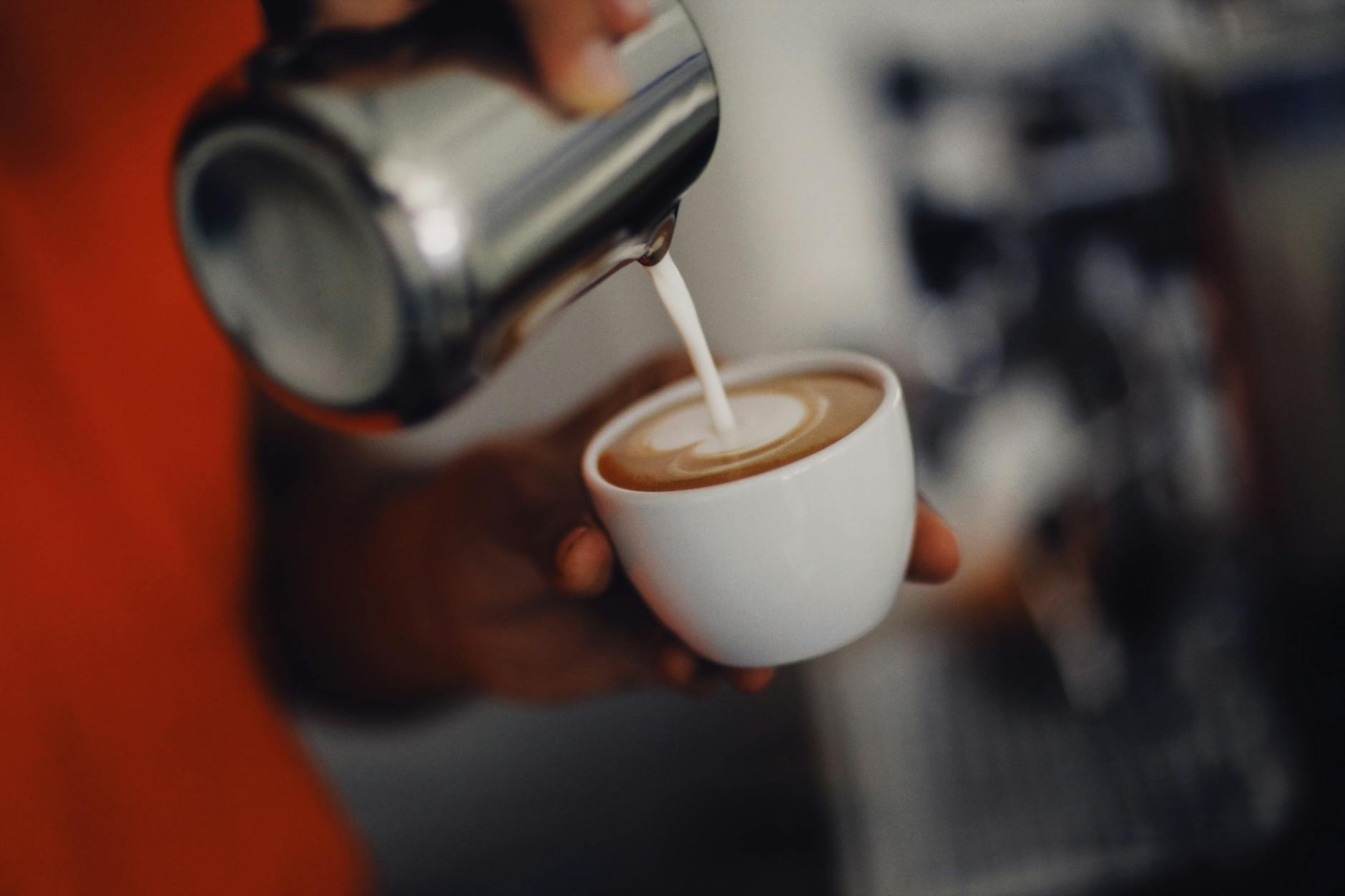 Barista creating latte art with steamed oat milk in a chai latte
