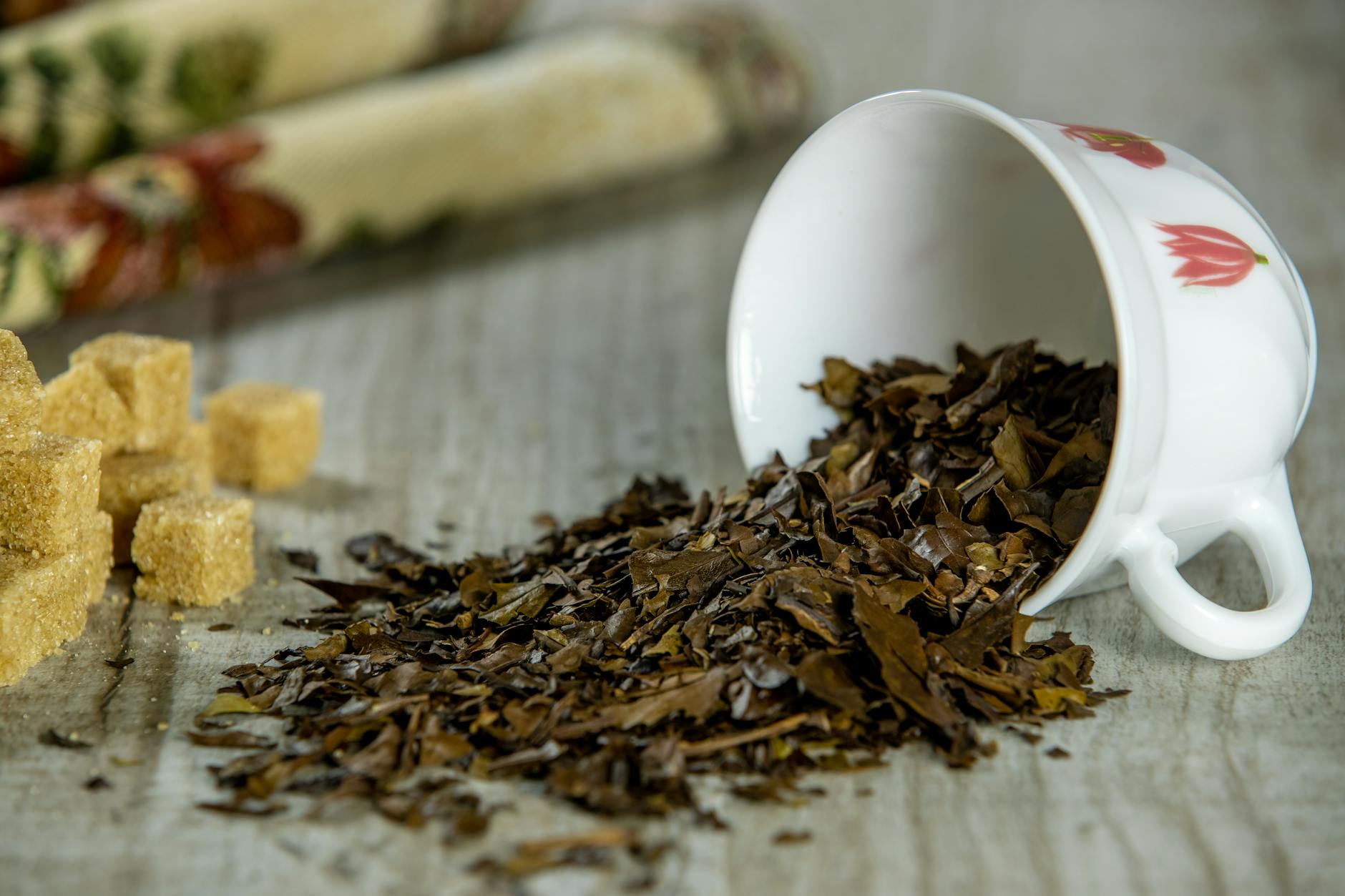 Loose tea leaves spilling from a teacup with sugar cubes, showing the base of chai caffeine