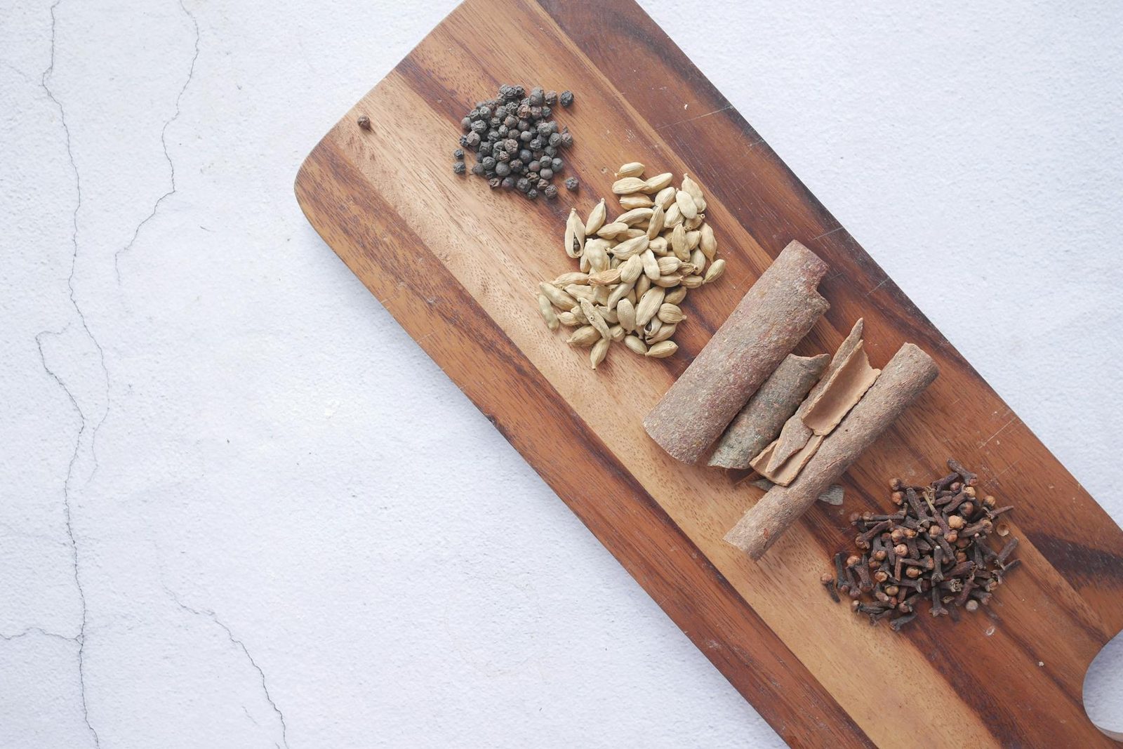 Flat lay of whole chai spices — cardamom, cinnamon, cloves, and black peppercorns on a cutting board