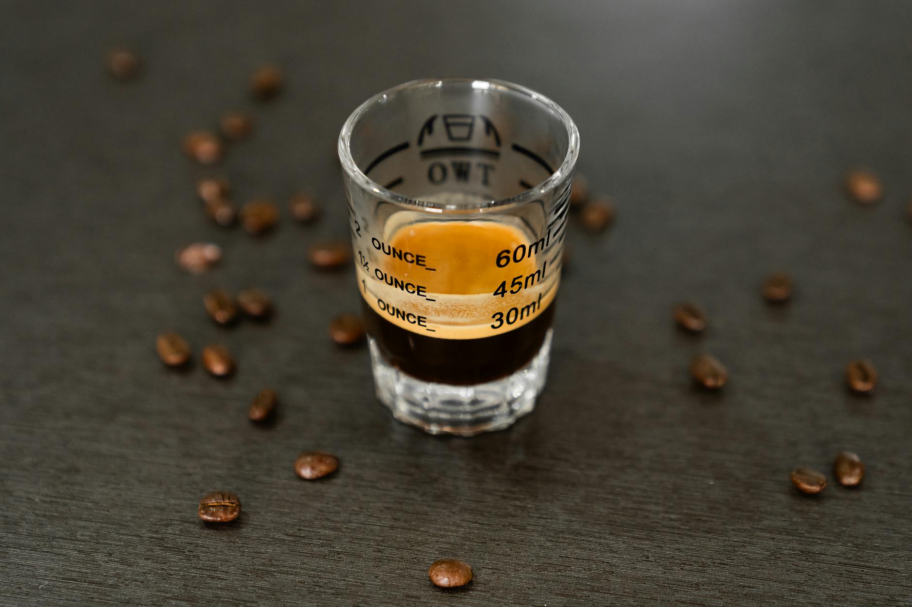 Espresso shot in a measurement glass with scattered coffee beans — the key ingredient that makes a chai dirty